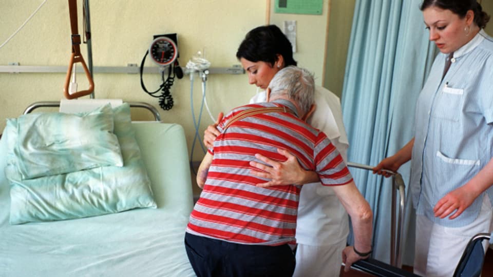Pflegefachfrauen helfen einer älteren Person ins Spitalbett