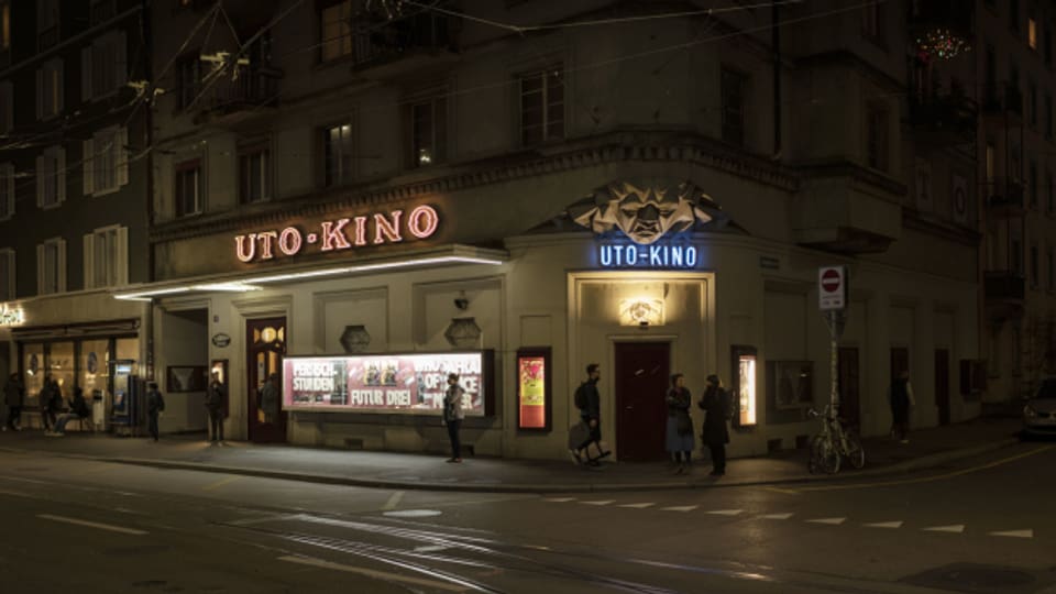 Das Kino Uto an der Kalkbreite in einer Aufnahme bei Nacht - roter Schriftzug, blau beleuchtete Skulptur über der Türe