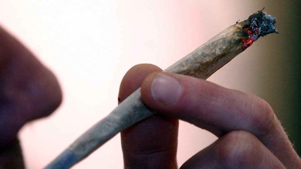 Ein rauchender Cannabis-Joint, gehalten von einer Hand