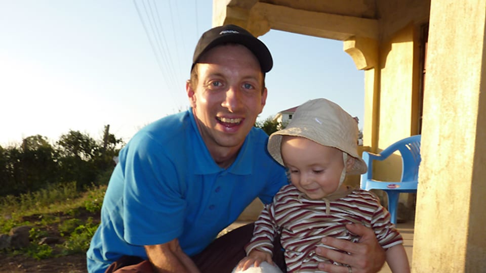 Andres Wirz mit seinem Sohn Nils (15 Monate) vor dem Haus eines Nachbarn in Abura.