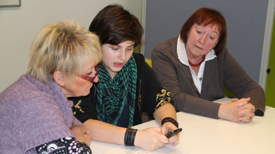 Jugendliche zeigen Seniorinnen und Senioren, wie man Apps auf einem Tablet-Computer anwendet.