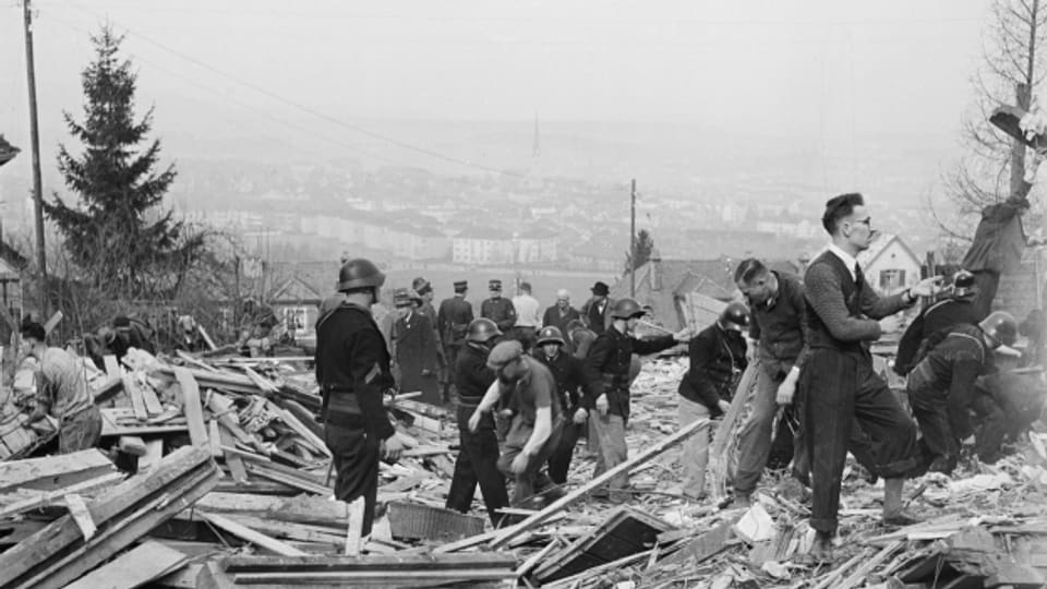 Luftschutzsoldaten und Zivilisten sind bei Rettungs- und Räumungsarbeiten auf einem Trümmerfeld in Zürich im Einsatz.