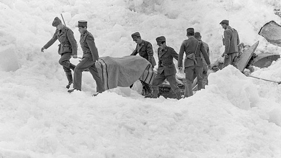 Soldaten und ein Polizist bergen ein Opfer auf dem zerstörten Barackenlager der Baustelle des Mattmarkstausees nach dem Niedergang einer Eislawine am 30. August 1965.