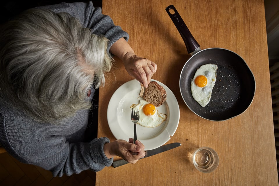 Eine ältere Frau isst Spiegeleier in ihrer Wohnung in der Zentralschweiz