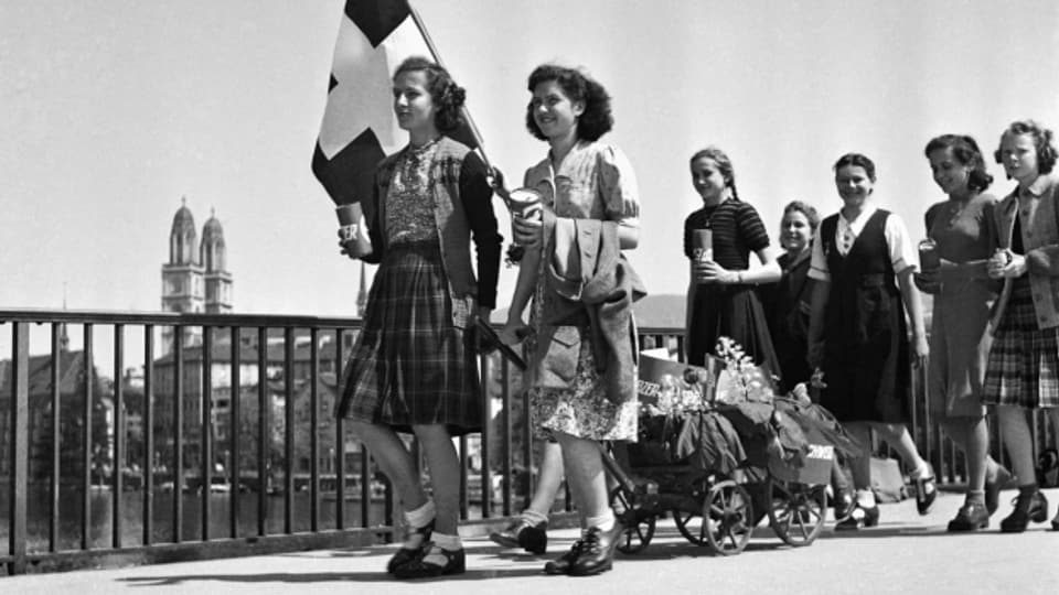 Mädchen ziehen am 8. Mai 1945 mit einer Schweizer Fahne und einem geschmückten Leiterwagen durch Zürich und sammeln Geld.