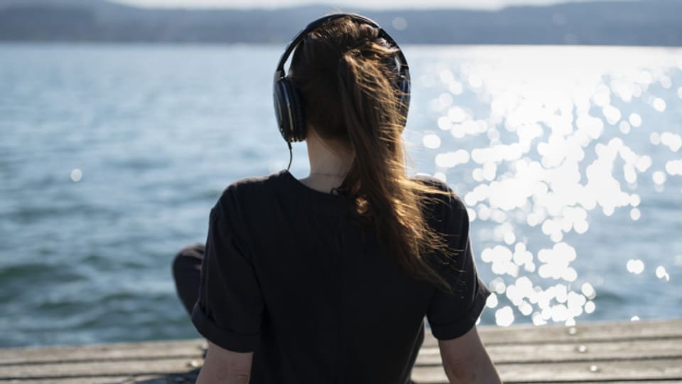 Eine junge Frau sitzt am Wasser mit dem Kopfhörer