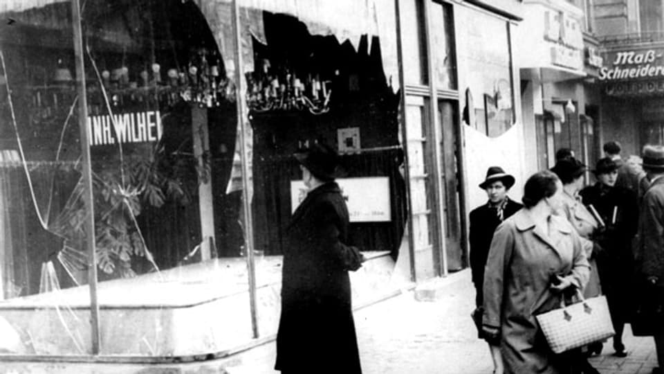 Passanten stehen vor einem jüdischen Geschäft, dessen Schaufenster während der Kristallnacht eingeschlagen wurden.