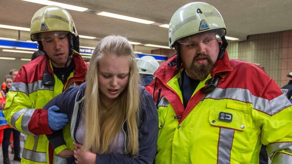 Eine Schauspielerin und zwei Feuerwehrmänner bei einer Krisensimulation zu Übungszwecken