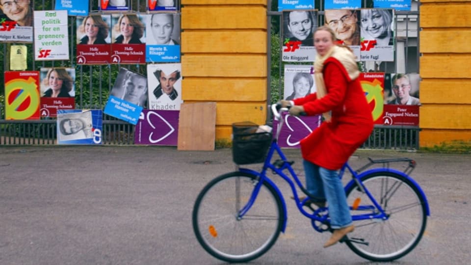 Eine Frau in Kopenhagen fährt an Wahlplakaten vorbei.