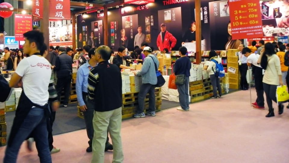 Eine Buchmesse in Taiwan: Leute stehen um Bücher herum und schauen sie an.