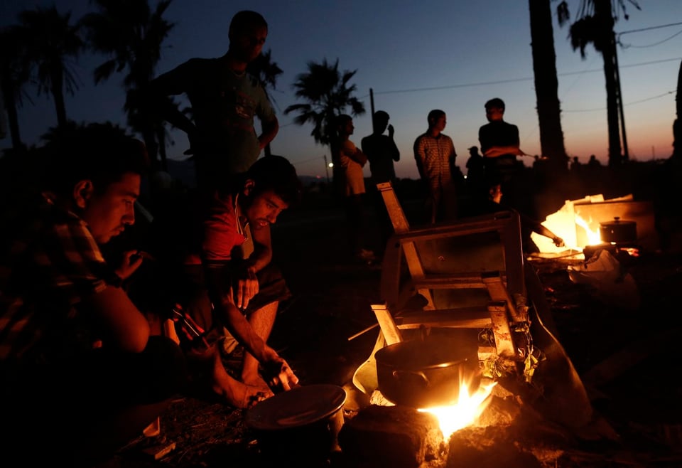 Flüchtlinge machen ein Feuer. Im Hintergrund geht die Sonne unter