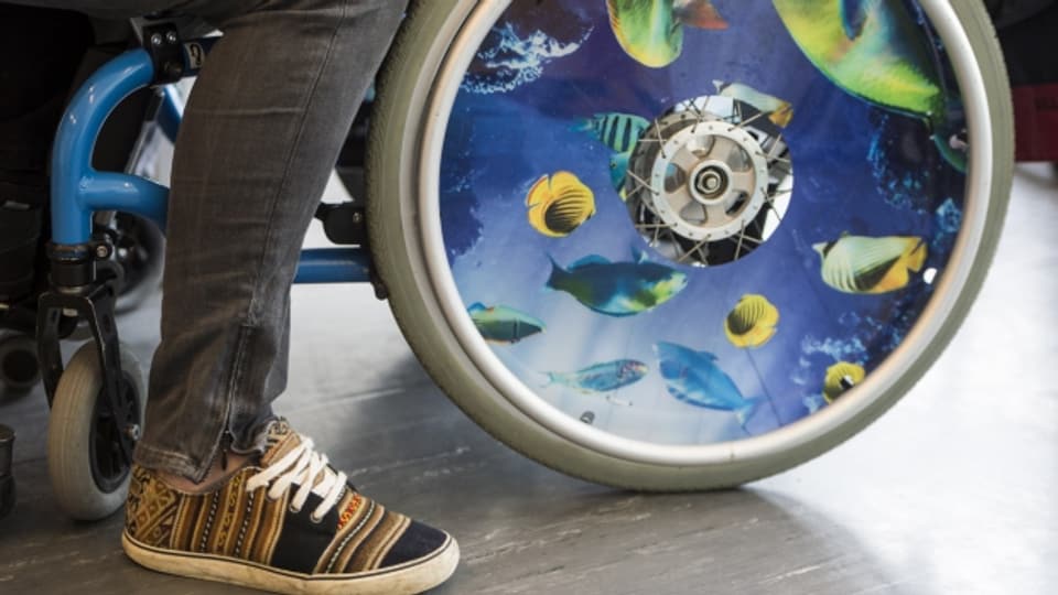 Mann im Rollstuhl mit bunten Fischen auf einem Rad