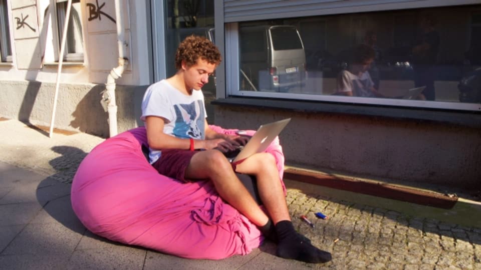 Symbolbild: Ein junger Mann sitzt drausen auf einem Sitzsack und arbeitet am Computer.