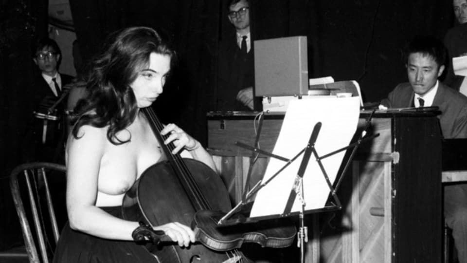 Charlotte Moorman spielt oben ohne und mit einer Geige als Bogen Cello.