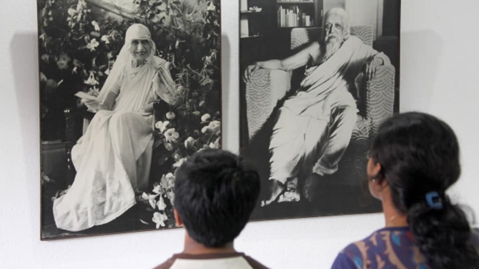 Zwei Personen stehen vor den Portraits der Auroville-Gründerin