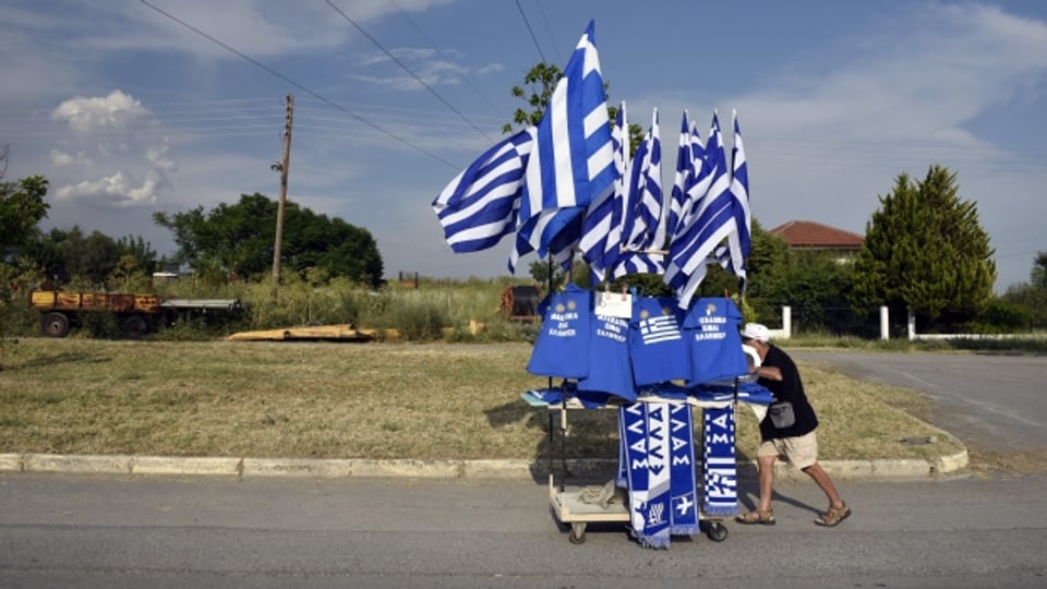 Ein Mann schiebt einen Wagen voll griechischer Flaggen.
