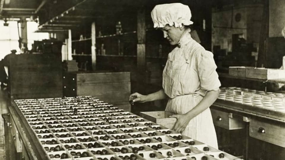 Ein altes Foto (ca. 1920) einer Frau, die in einer Schokoladenfabrik Schokostücke sortiert