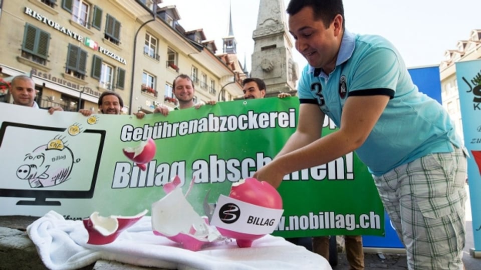 Anian Liebrand, Präsident Junge SVP Schweiz, zertrümmert das Billag-Sparschwein.