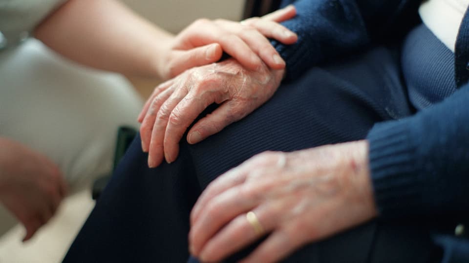 Das Adieu-Sagen begleiten: Eine Pflegerin hält die Hand einer Seniorin in einem Schweizer Pflegeheim.