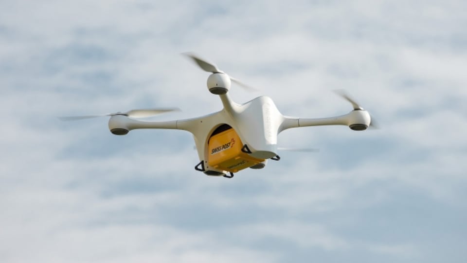Eine Drohne transportiert ein gelbes Post-Paket.