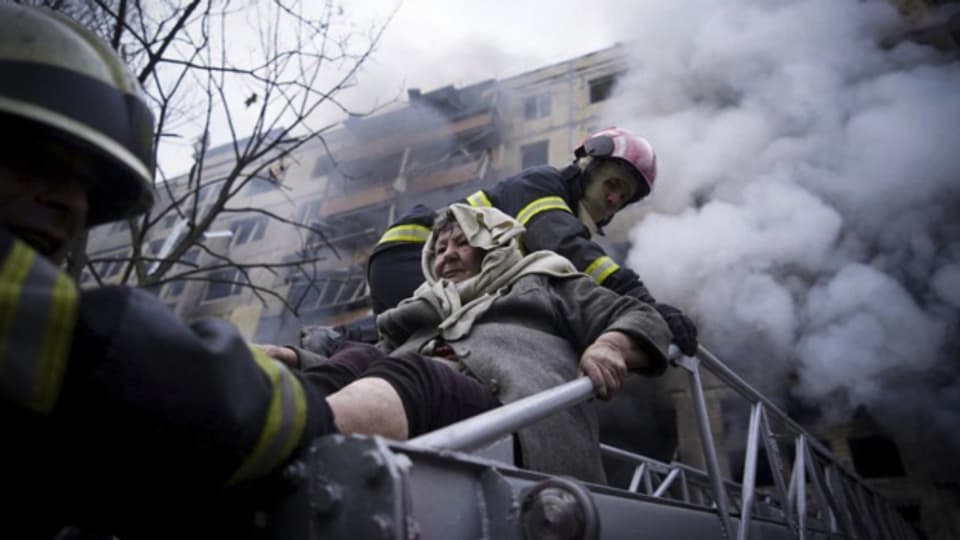 Feuerwehrleute evakuieren eine ältere Frau aus einem von Granaten getroffenen Wohnhaus in Kiew.