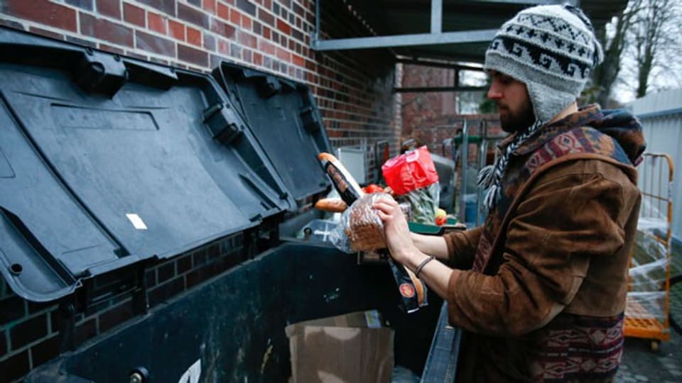 Ein junger Mann prüft Produkte aus einem Abfallcontainer.