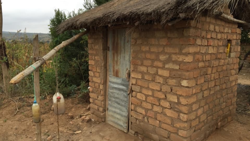 Eine neu gebaute Latrine in Tansania, davor eine einfache Einrichtung, um die Hände waschen zu können.