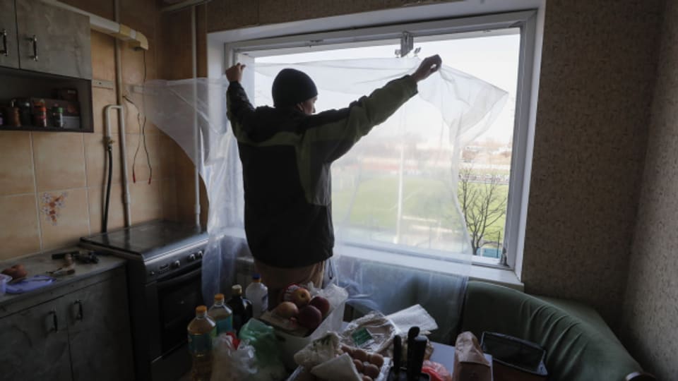 Ein Bewohner Kiews versucht das Fenster seiner beschossenen Wohnung mit einer Plastikfolie abzudecken.