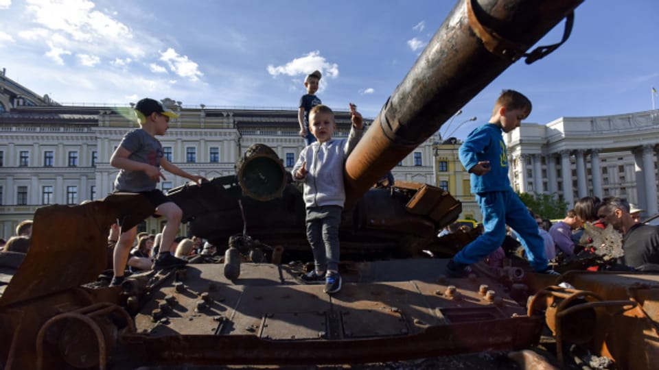 Kinder klettern auf einen ausgebrannten russischen Panzer, der als Mahnmal auf einem Platz in Kiew aufgestellt wurde.