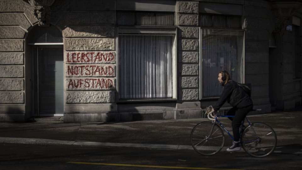 Eine Frau fährt ein Fahrrad vor einem Gebäude mit der Aufschrift "Leerstand, Notstand, Aufstand" am 9.3.2023 in Zürich.