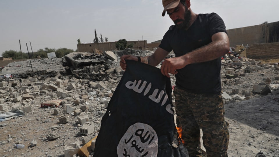  Der Kämpfer einer christlichen Miliz hält eine im syrischen Bürgerkrieg zurückgelassene IS-Flagge in den Händen. (Archivbild)