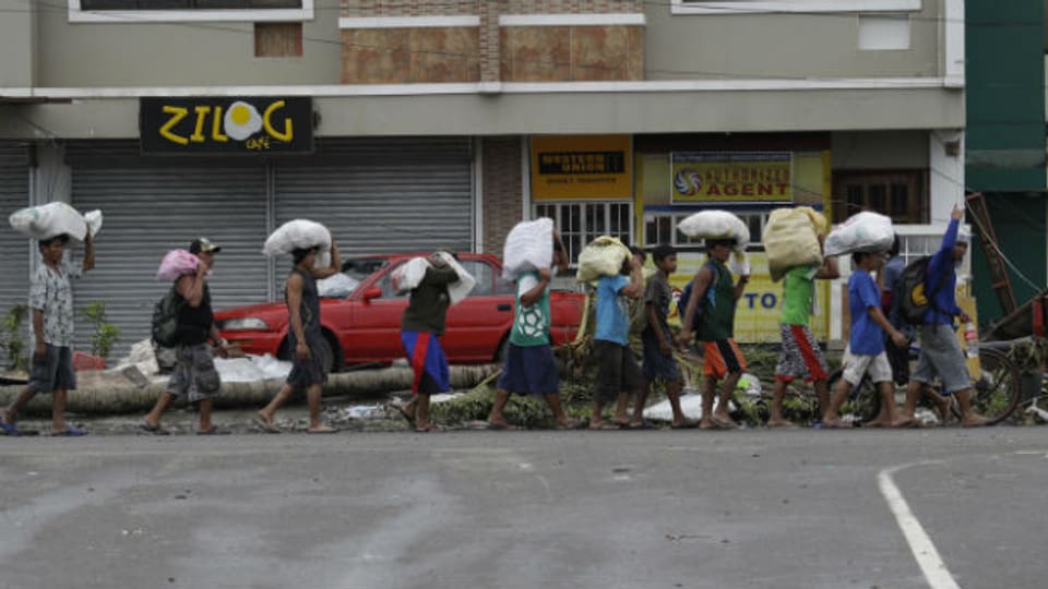 Opfer des Taifuns in Tacloban schleppen Säcke mit Hilfsgütern.
