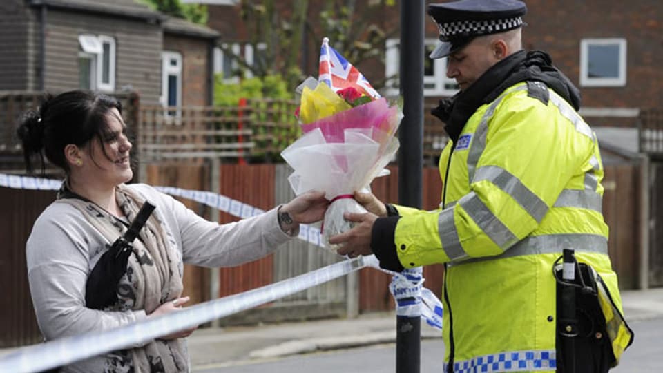 Eine Welt ohne Terrorismus habe es nie gegeben und es werde sie nie geben, meint der Anti-Terrorchef Mike Smith. Bild: Eine Frau überreicht einem Polizisten Blumen, dort wo 23. Mai ein Soldat brutal ermordet wurde.