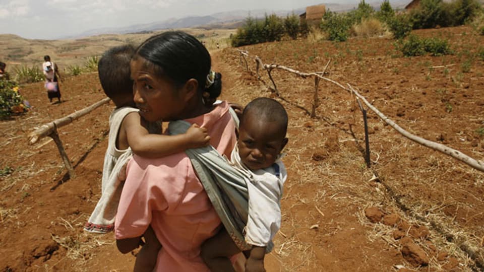  Eine afrikanische Frau trägt ihre Kinder nach Hause - nach stundenlangem Marsch nach dem Besuch in einer provisorischen Dorfklinik. In ihrem Dorf mangelt es an vielem: medizinische Versorgung. Schulen. Bildung. Es fehlt an Geld.