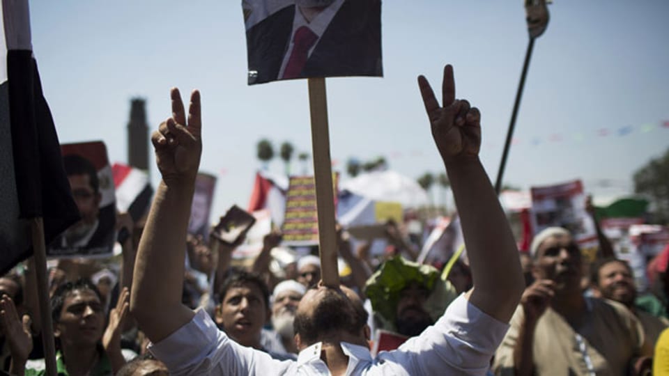 Ein Anhänger des gestürzten Präsidenten Ägyptens Mohammed Mursi macht das Victory-Zeichen, während er ein Banner auf dem Mund balanciert während einer Protestaktion in der Nähe der Universität von Kairo in Gizeh, Kairo, Ägypten, Freitag, 26. Juli 2013