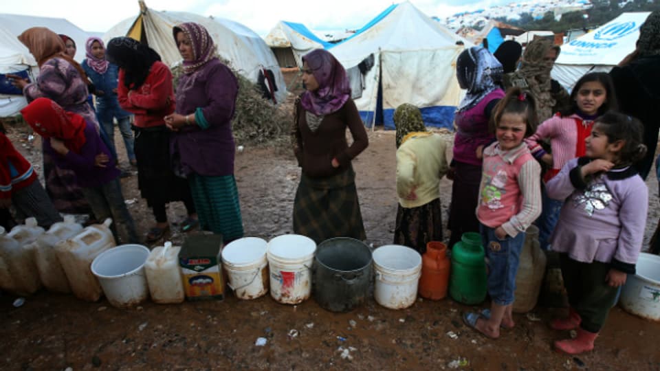 Syrische Flüchtlinge warten in einem Flüchtlingscamp darauf, ihre Eimer mit Wasser zu füllen.