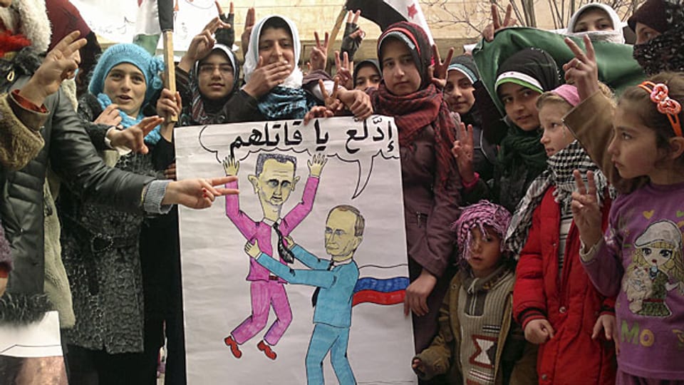 Proteste in einem syrischen Dorf bei Idlib. Die Karikatur sagt: «Russlands Putin sagt zu Syriens Assad: du kuschliger Volksmörder!»
