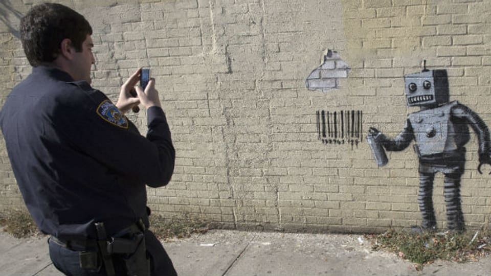 Ein Polizist fotografiert ein Graffiti des Künstlers Banksy.