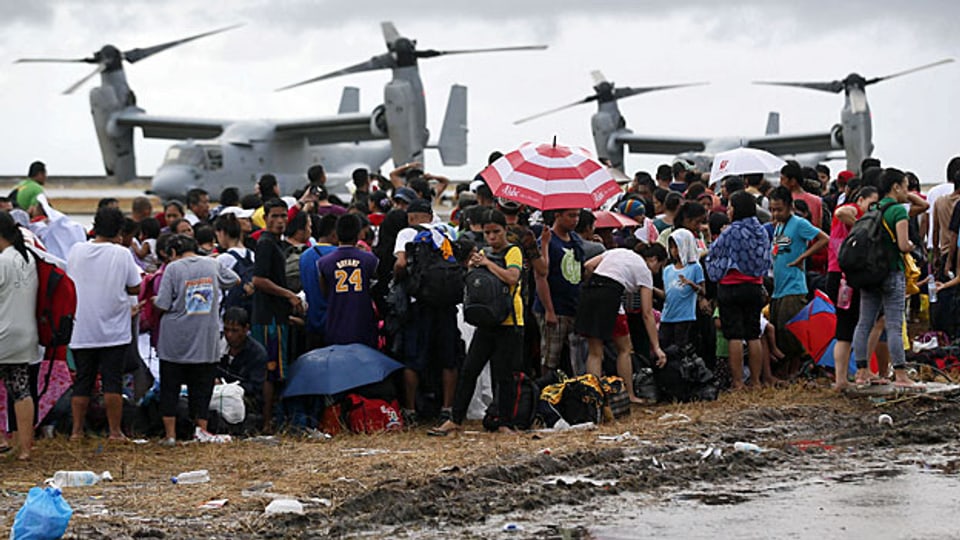 Menschen auf dem Flughafen Tacloban warten auf Evakuierung auf dem Luftweg; die Flugzeuge im Hintergrund kommen von einem Flugzeugträger der US-Marine.