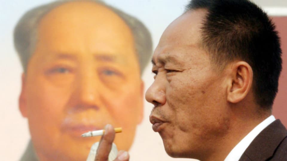 Ein Chinese raucht - im Hintergrund das Protrait von Mao.