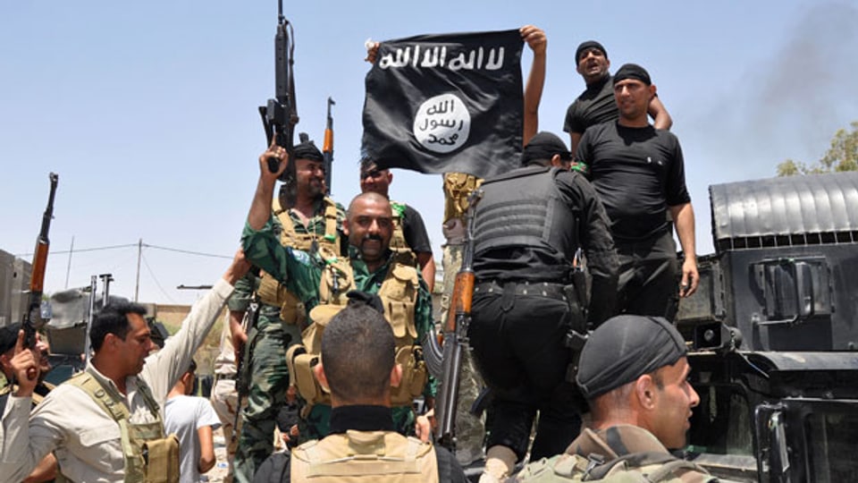 Irakische Soldaten halten eine erbeutete Flagge der ISIS in die Höhe.