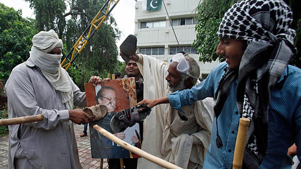 Protestierende in Islamabad treten ihren Präsidenten symbolisch mit Füssen; sie schlagen mit ihren Schuhen auf ein Portrait von Nawaz Sharif ein.