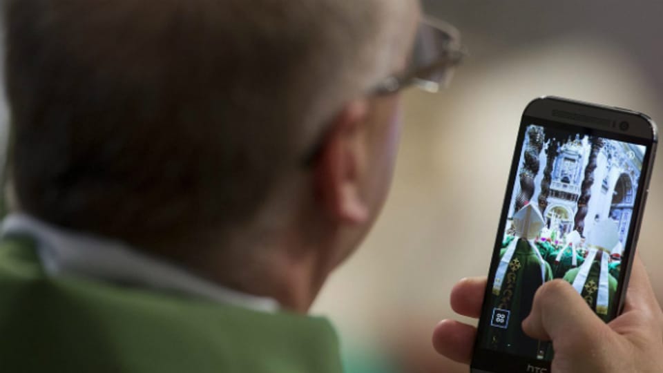 Ein Priester fotografiert den Papst bei der Messe am Sonntag mit seinem Handy.