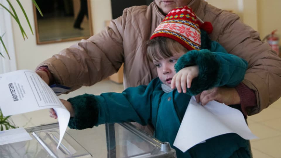 Wahlen in Luhansk: ein kleines Mädchen wirft den Stimmzettel der Grossmutter in die Urne.