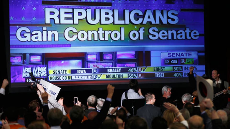 Republikanische Unterstützer jubeln vor einem riesigen TV-Bildschirm, der die positiven Ergebnisse zeigt.