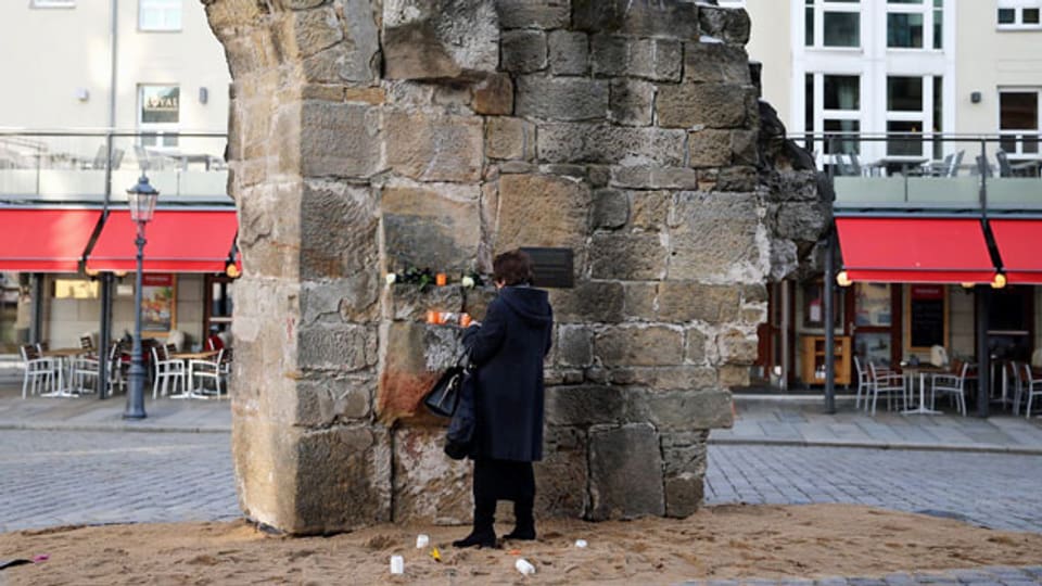 Überrest der zerstörten Frauenkirche in Dresden. Im Gedenken an die Zerstörung der Stadt im Zweiten Weltkrieg zündet diese Frau eine Kerze an.