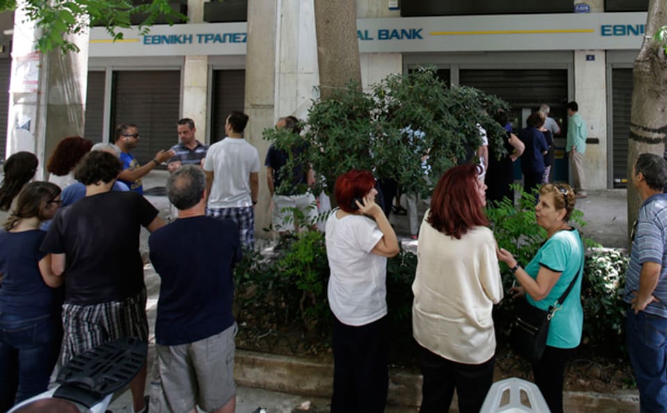 Griechische Bürgerinnen und Bürger debattieren die jüngste Entwicklung vor einem Bancomaten im Zentrum Athens