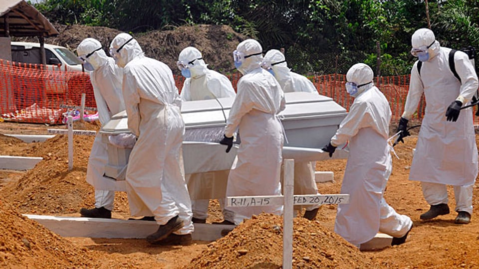 Gesundheitsarbeiter in weissen Schutzanzügen tragen den Sarg eines Ebola-Opfers auf einen Friedhof. Im März 2015 in der liberianischen Hauptstadt Monrovia.