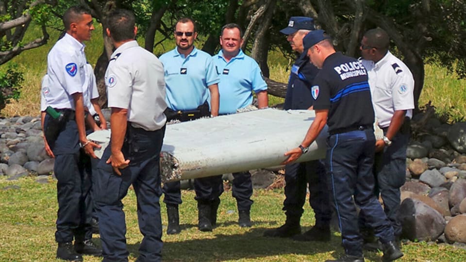 Beamte tragen das in La Réunion gefundene Wrackteil eines Flugzeuges weg. Nun wird untersucht, ob es zur verschwundenen Maschine der Air Malaysia gehört.