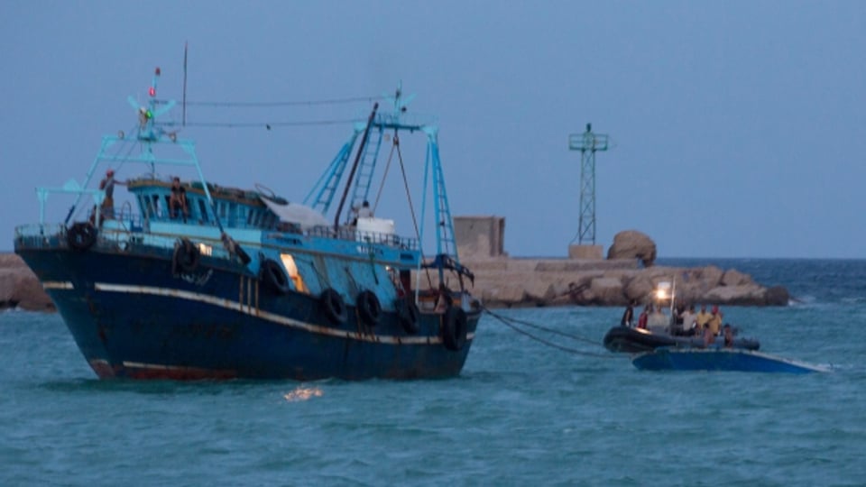 Ein Fischkutter schleppt ein kleines Boot mit Flüchtlingen vor der Küste Libyens ab.